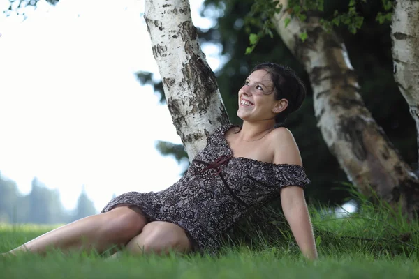 Hübsche junge Frau sitzt auf einem Rasen in einem Park — Stockfoto