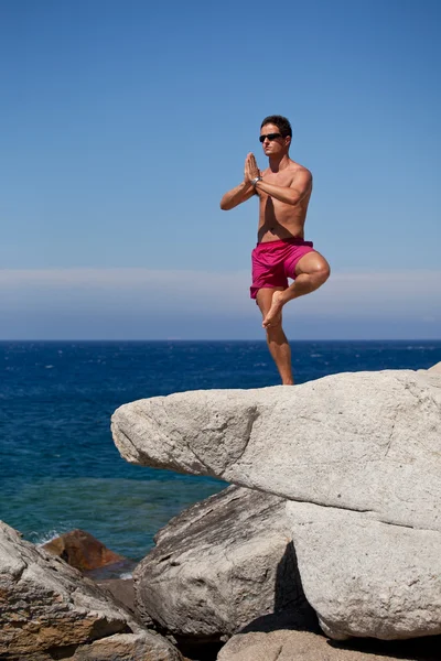 Knappe jongeman mediteren op een zonnige rotsachtige strand — Stockfoto