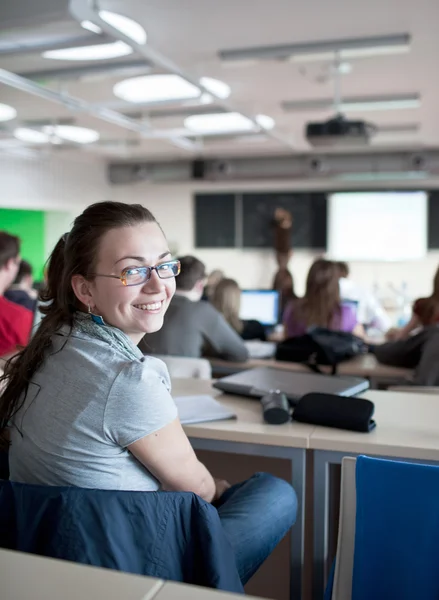 Ung ganska kvinnliga collegestudent sitter i ett klassrum — Stock fotografie