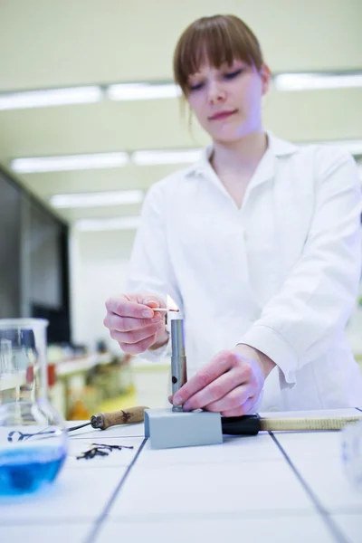 Young and pretty female researcher lighting up a burner in a lab — Stock Photo, Image