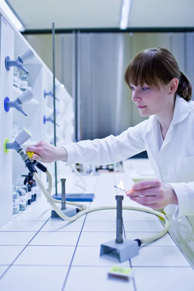 Young and pretty female researcher lighting up a burner in a lab — Stock Photo, Image