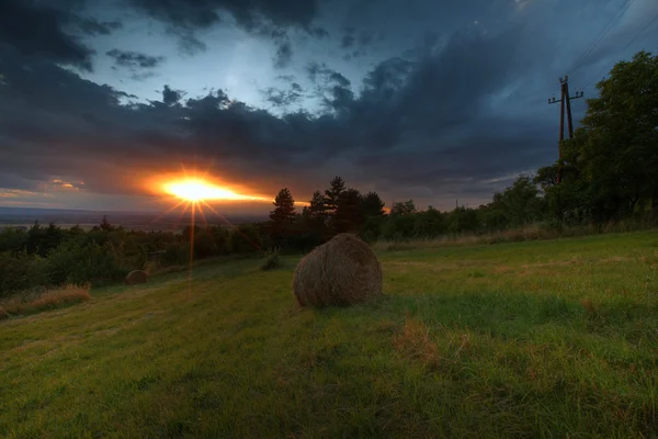 Kleine veld met Balen stro bij zonsondergang. — Stockfoto