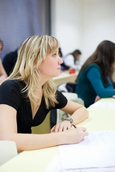 Fiatal csinos női főiskolai hallgató ül egy osztályteremben — Stock Fotó