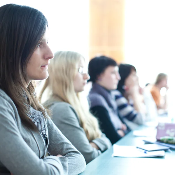 Young pretty female college student sitting in a classroom full — Stock Photo, Image