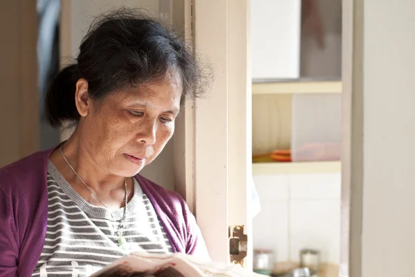 stock image A 50s asian woman reading newspaper at home