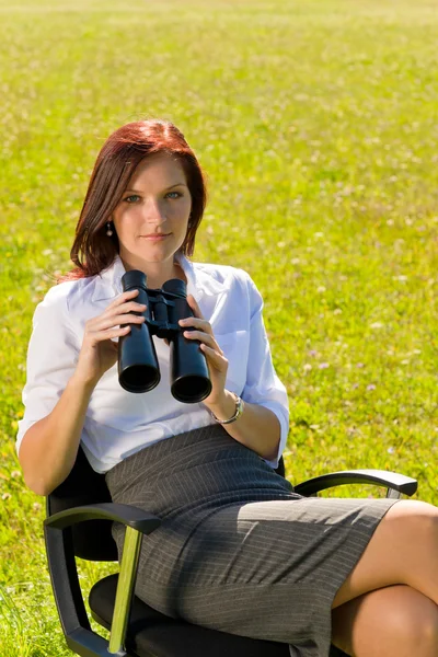 Empresária sentar-se no prado ensolarado procurar binocular — Fotografia de Stock