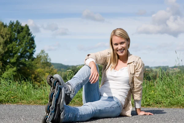 Вбудовані ковзани молода жінка сидить асфальтованою дорогою — стокове фото