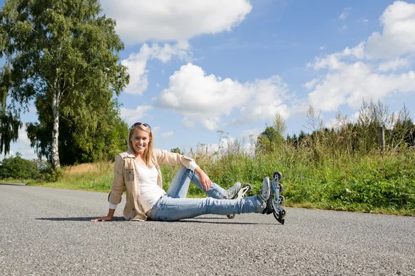 インライン スケートの若い女性のアスファルトの道路に座って — ストック写真