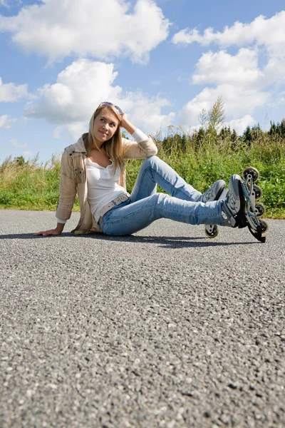 坐在沥青混凝土路面的内联溜冰鞋年轻女人 — 图库照片