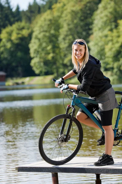Молодая горная велосипедистка, стоящая у озера — стоковое фото