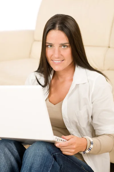 Žena s laptopem sedí gauč s úsměvem — Stock fotografie