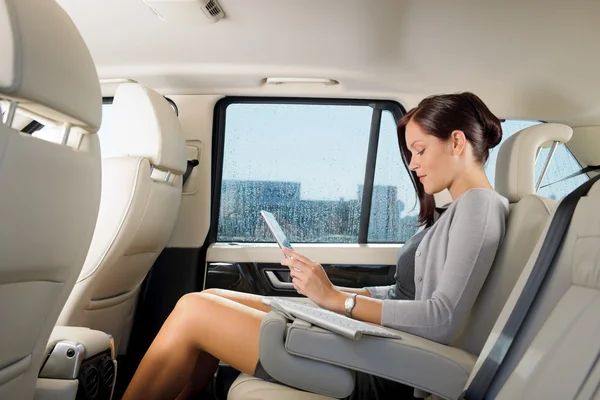 Geschäftsfrau im Auto tippt Tablet an Stockbild