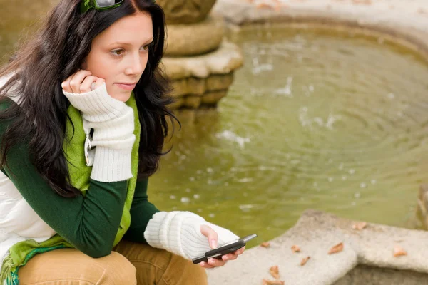 Herbstlicher Parkbrunnen junge Frau hält Handy in der Hand — Stockfoto