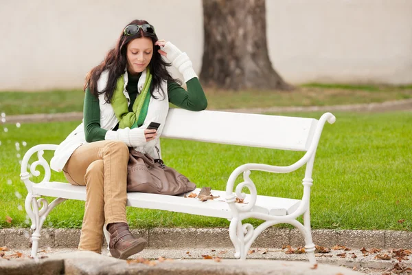 Скамейка в Осеннем парке, молодая женщина держит телефон — стоковое фото