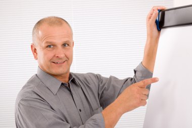 Mature businessman pointing at empty flip chart clipart