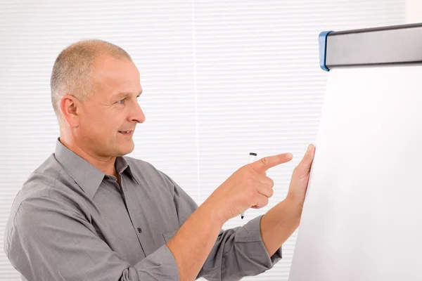Mature businessman writing at empty flip chart — Stock Photo, Image