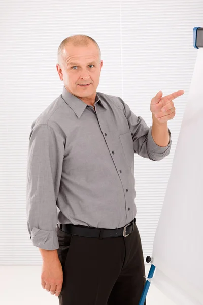 Mature businessman pointing at empty flip chart — Stock Photo, Image