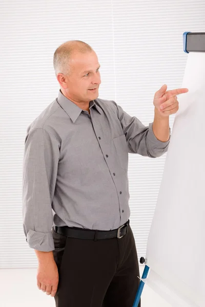Mature businessman pointing at empty flip chart — Stock Photo, Image