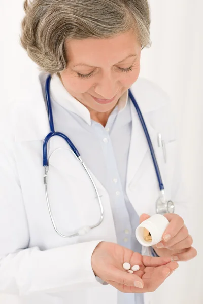 Старший лікар жінка тримає таблетки, дивлячись вниз — стокове фото