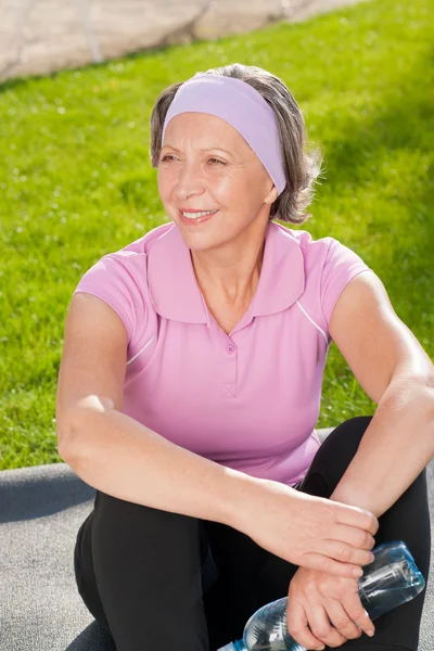 Senior sportieve vrouw zitten op mat zonnige — Stockfoto