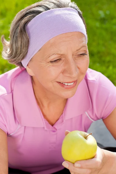 Starší žena sportive úsměv jíst jablko venkovní — Stock fotografie
