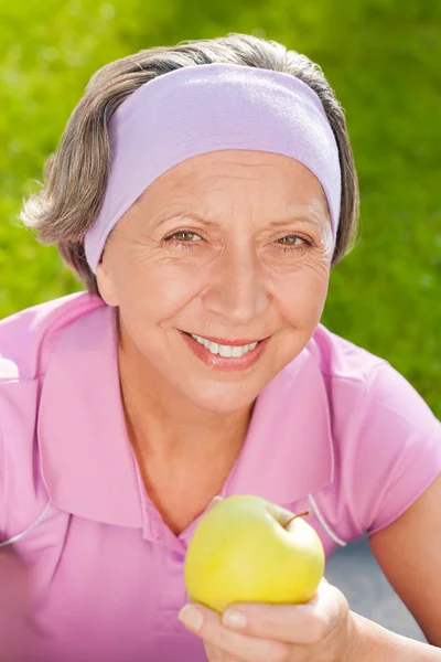Старшая спортивная женщина улыбка есть яблоко на открытом воздухе — стоковое фото