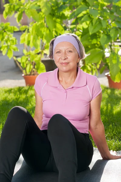 Старша спортивна жінка сидить на килимку сонячно — стокове фото