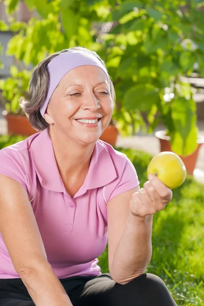 Senior sportos asszony mosoly enni almát szabadtéri — Stock Fotó