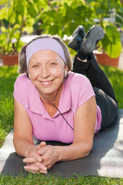 Senior mulher esportiva ouvir música no tapete — Fotografia de Stock