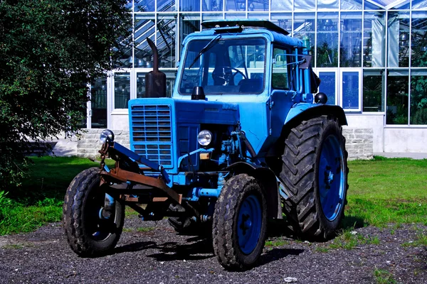 Painted in blue tractor standing before building — Stock Photo, Image