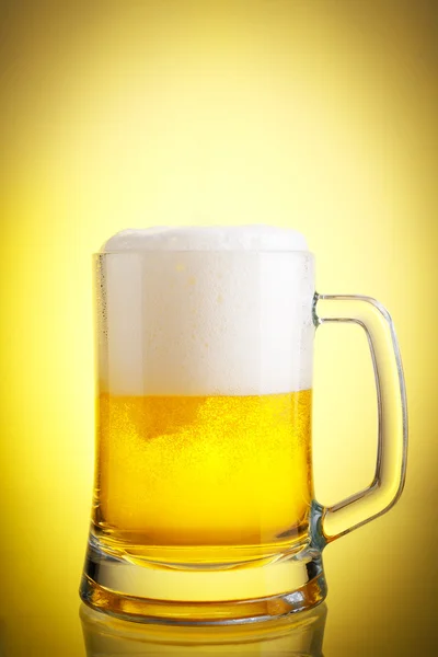 Glass of beer close-up with froth over yellow background — Stock Photo, Image