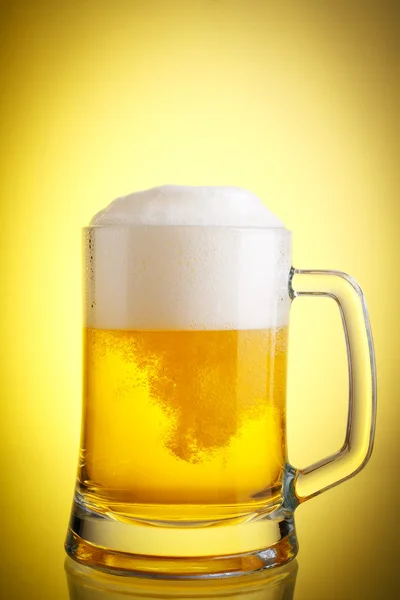 Glass of beer close-up with froth over yellow background Stock Image
