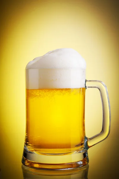 Glass of beer close-up with froth over yellow background Stock Picture