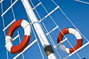 Sailing mast with life buoy over blue sky clipart