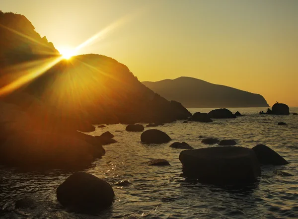 O sol sobe por causa de uma rocha sobre o mar Fotos De Bancos De Imagens