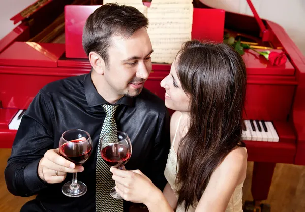 Casal com copos de vinho perto do piano — Fotografia de Stock