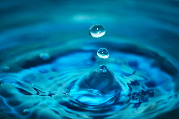 Droppar falla i det blå vattnet — Stockfoto
