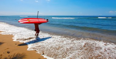 Surfer or boeard puddler walking on the beach in to the tropical ocean. Mau clipart