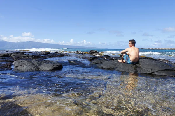 Mladý muž sedí na lávové kameny u oceánu v kapalua beach, maui. Hawa — Stock fotografie