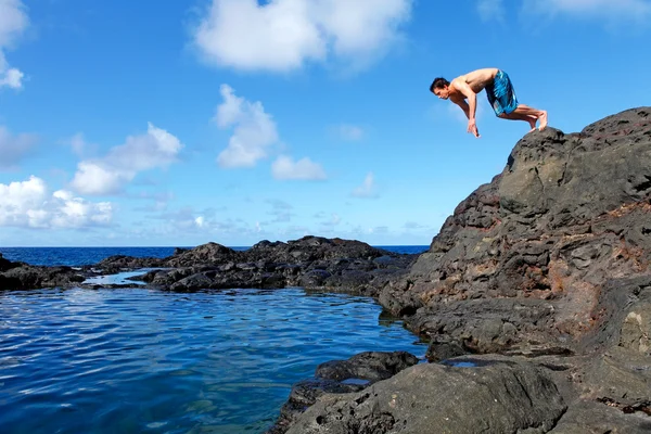 Junger Mann springt von der Klippe ins Wasser. — Stockfoto