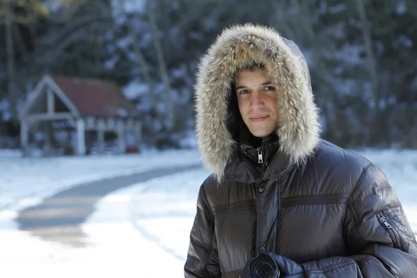Young man in furry winter coat in the snow park. — Stock Photo, Image