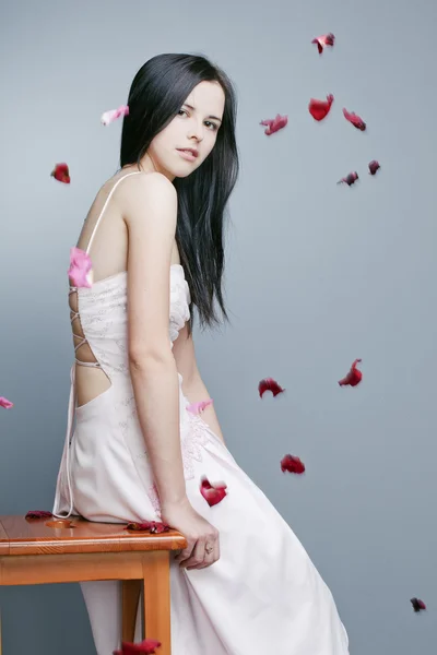 Mooi meisje met perfecte huid in een lange jurk met rozenblaadjes — Stockfoto