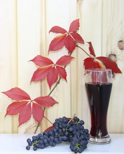 stock image A glass with wine and grapes against red leaves and a wooden wall