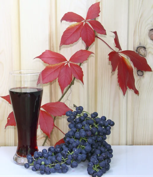 stock image A glass with wine and grapes against red leaves and a wooden wall