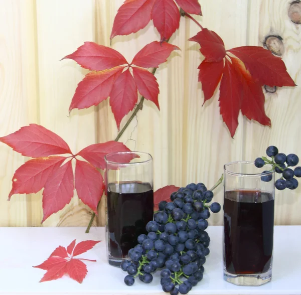 Two glasses with wine and grapes against red leaves and a wooden wall — Stock Photo, Image