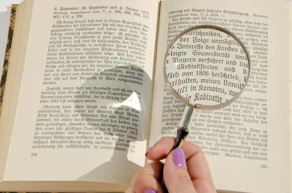 Mão de mulher segurando lupa sobre a página do livro alemão . — Fotografia de Stock