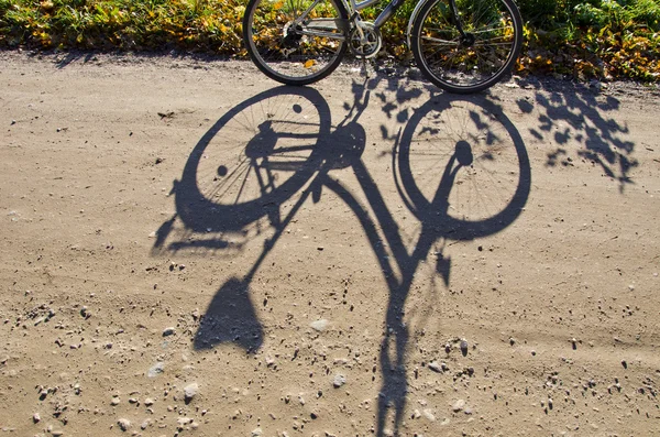 Standing bicycle shadow on gravel road. — Stok fotoğraf
