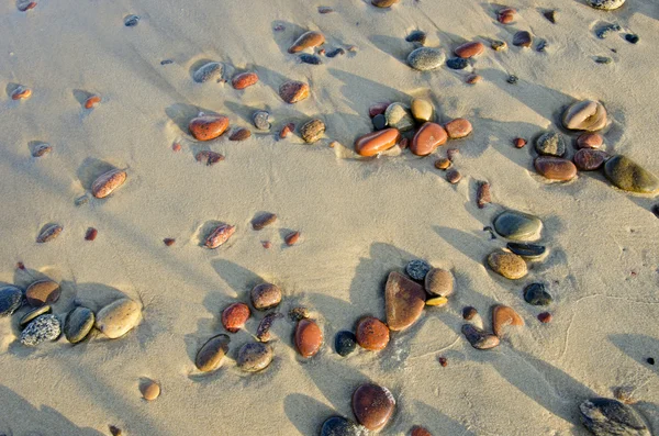 Kleurrijke natte keien rubed door golven in zee zand. — Stockfoto