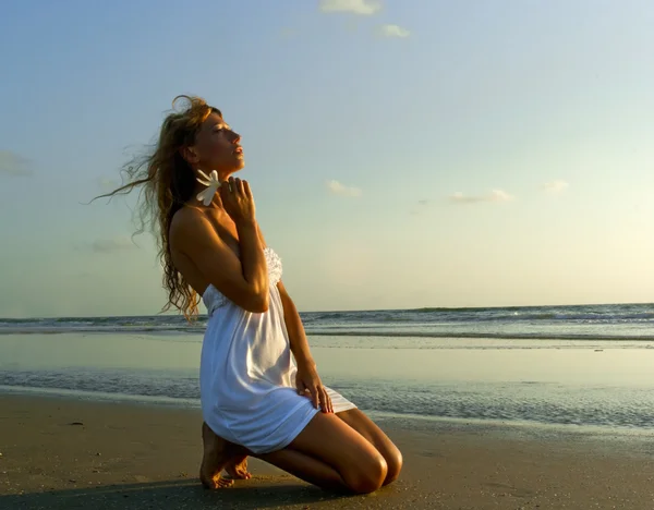 Underbara kvinna i vit klänning knäböja på stranden — Stockfoto