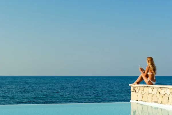 Mulher de biquíni branco sentado perto da piscina infinita — Fotografia de Stock